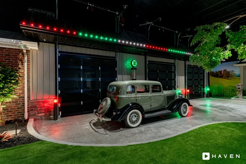 A classic car parked in front of a garage with red, green and white permanent lights along the roofline.