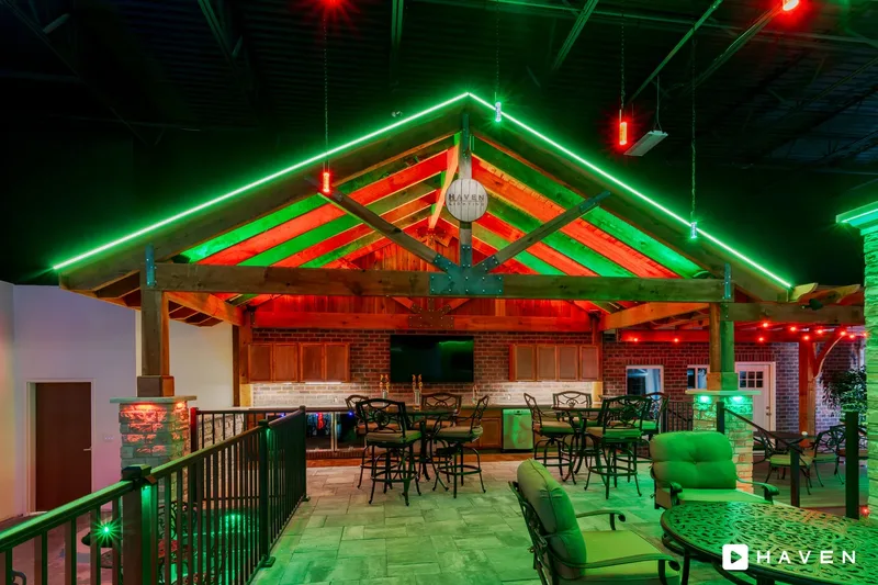 A covered outdoor bar and patio with green roofline lighting and red and green lights on the wood beams.