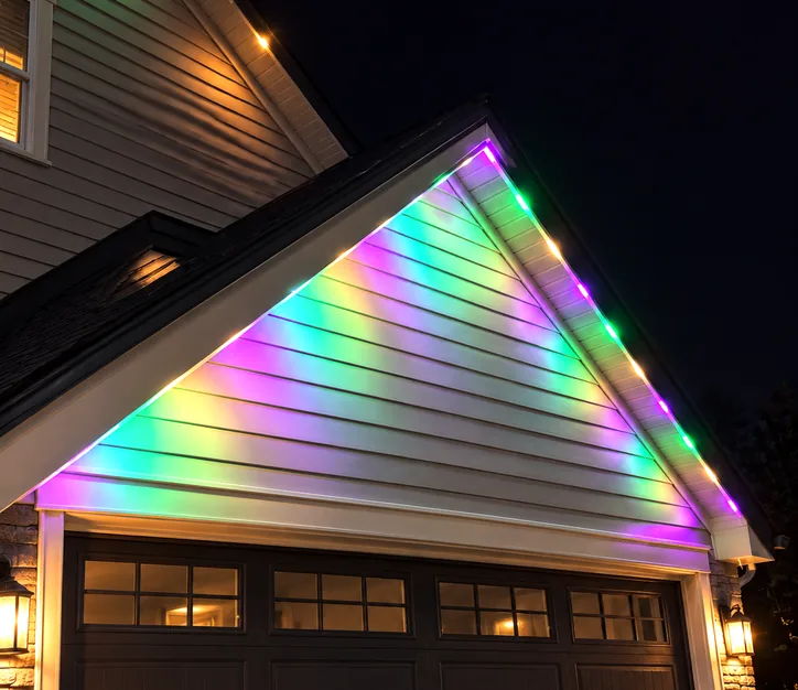 A garage gable lit with purple, green and warm white permanent lights.