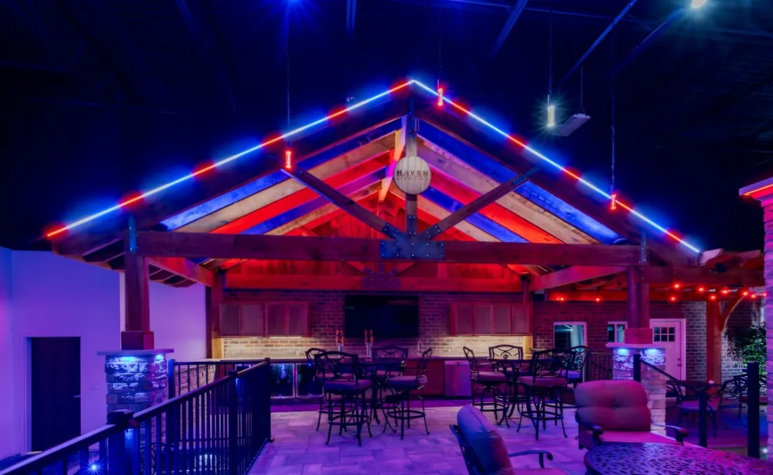 A covered outdoor bar and patio with red, white and blue permanent lighting along the roof trusses.