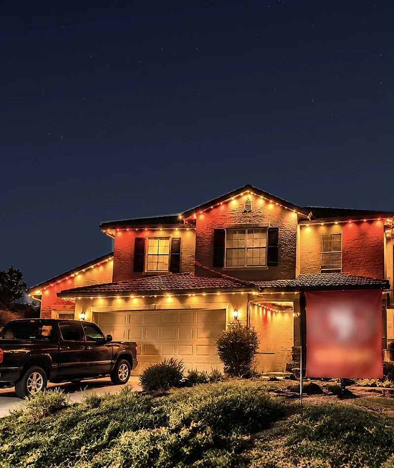 A two-story home lit in red and gold game-day colors along every roofline, with a team flag in the yard.