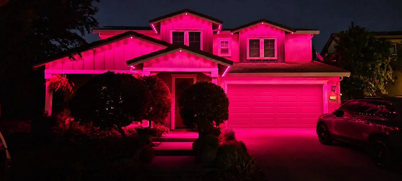 A two-story home washed in hot pink from permanent lights along every roofline.
