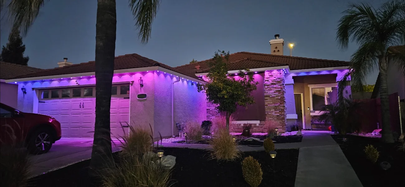 A tile-roof ranch home with purple and blue permanent lights along the eaves, washing the garage and stone entry.