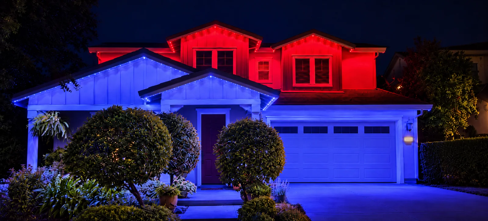 A two-story home with red permanent lights on the upper rooflines and blue on the lower rooflines and garage.
