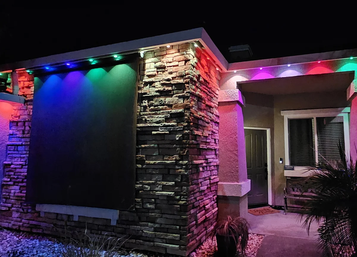 A stone front and entry lit in blue, purple, green, red and pink by permanent lights under the eave.